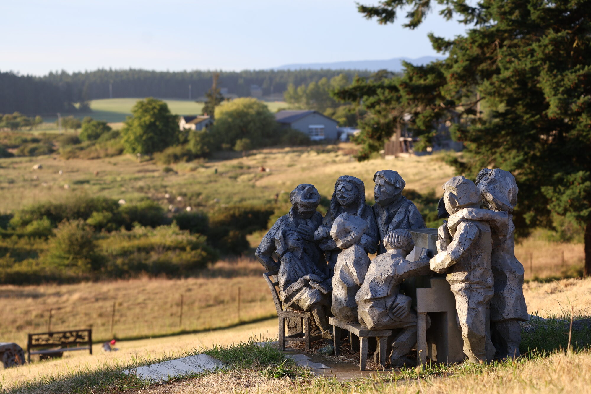 Stone sculptures of people gathered around a table on a golden hillside